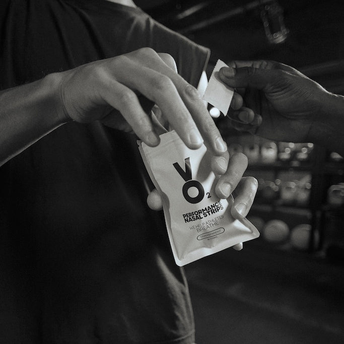 Two people exchanging a pack of VO2 Nasal Strips in a gym setting.